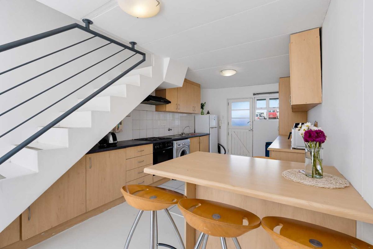 Compact kitchen featuring light wood cabinetry, built-in oven, gas hob, and a breakfast bar, situated beneath an open staircase.