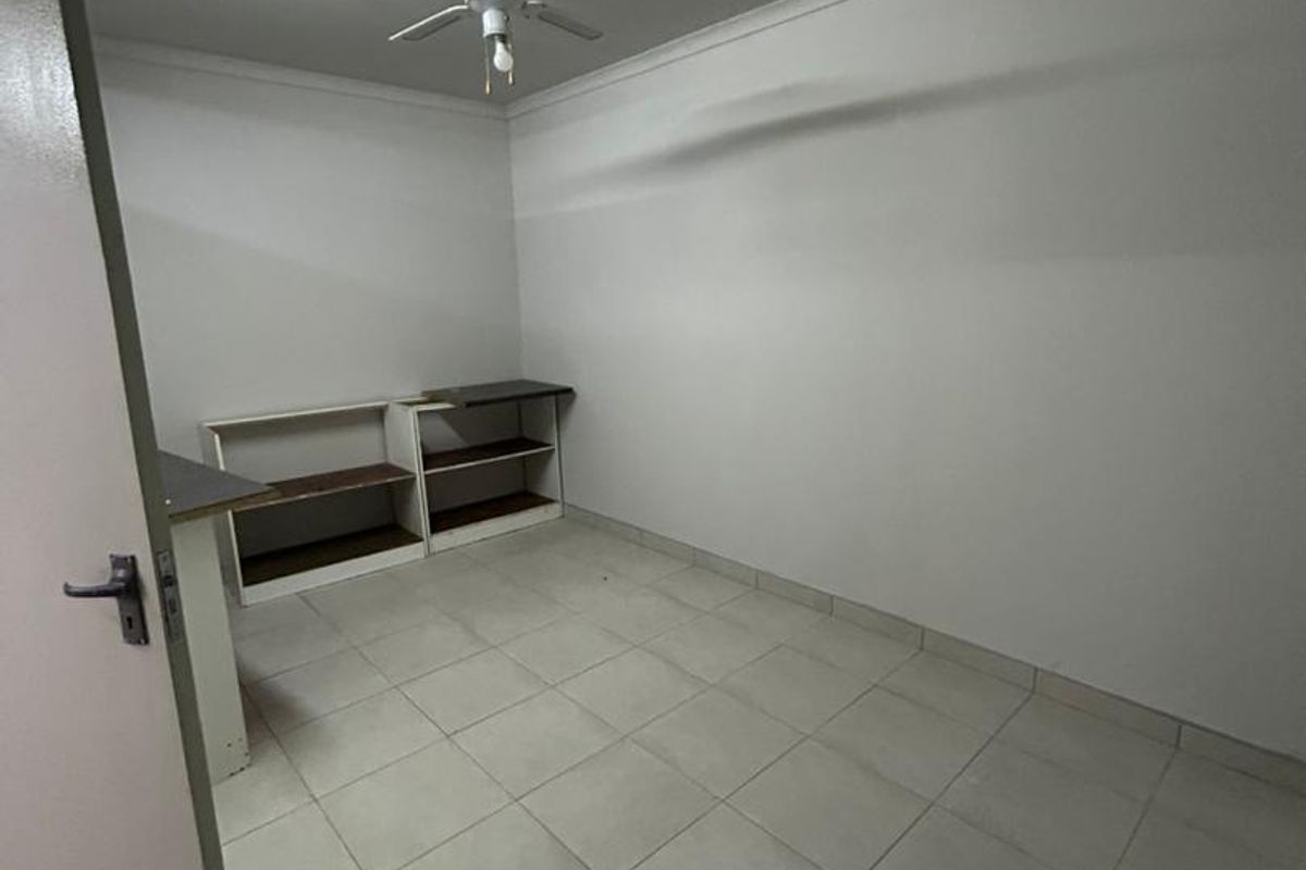 A simple, empty bedroom featuring tiled flooring, a ceiling fan, and built-in shelving units, providing a blank canvas for personalization.
