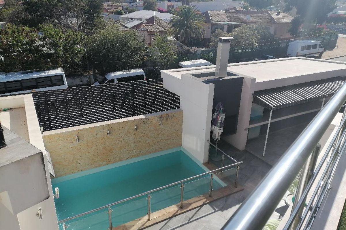 Elevated view of a modern pool area featuring a tiled deck, stone-clad feature wall, built-in braai, and stainless steel balustrades.