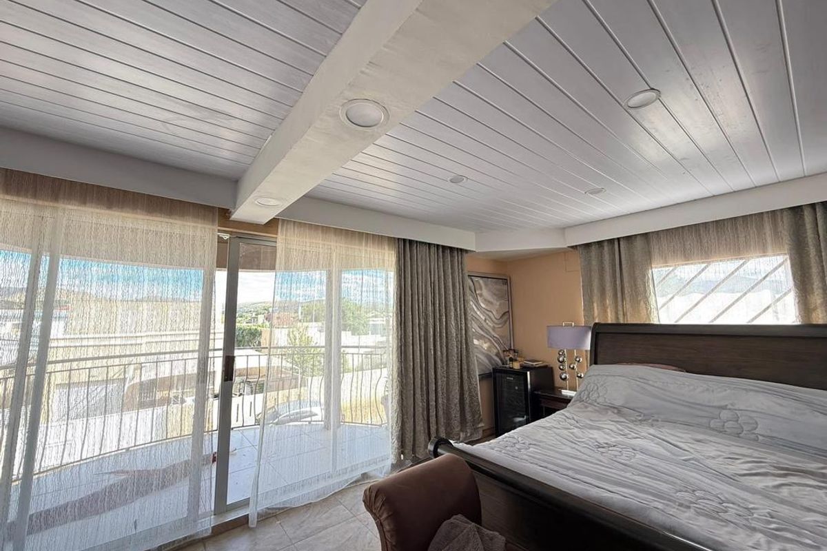 Spacious bedroom featuring a white timber-paneled ceiling with recessed lighting and large sliding glass doors opening onto a private balcony.