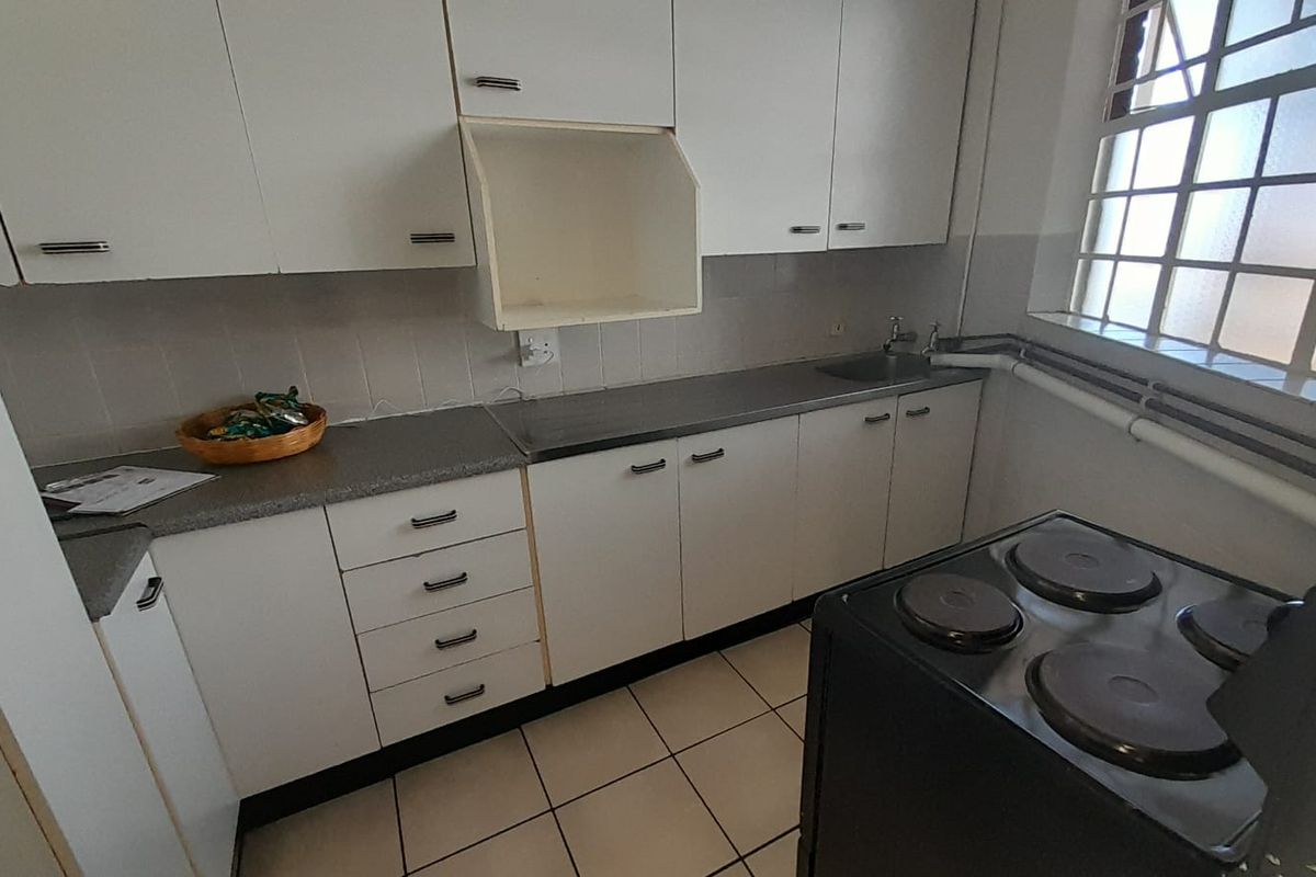 A functional kitchen featuring white cabinetry, laminate countertops, a stainless steel sink, and tiled flooring, providing a practical workspace for daily meal preparation.