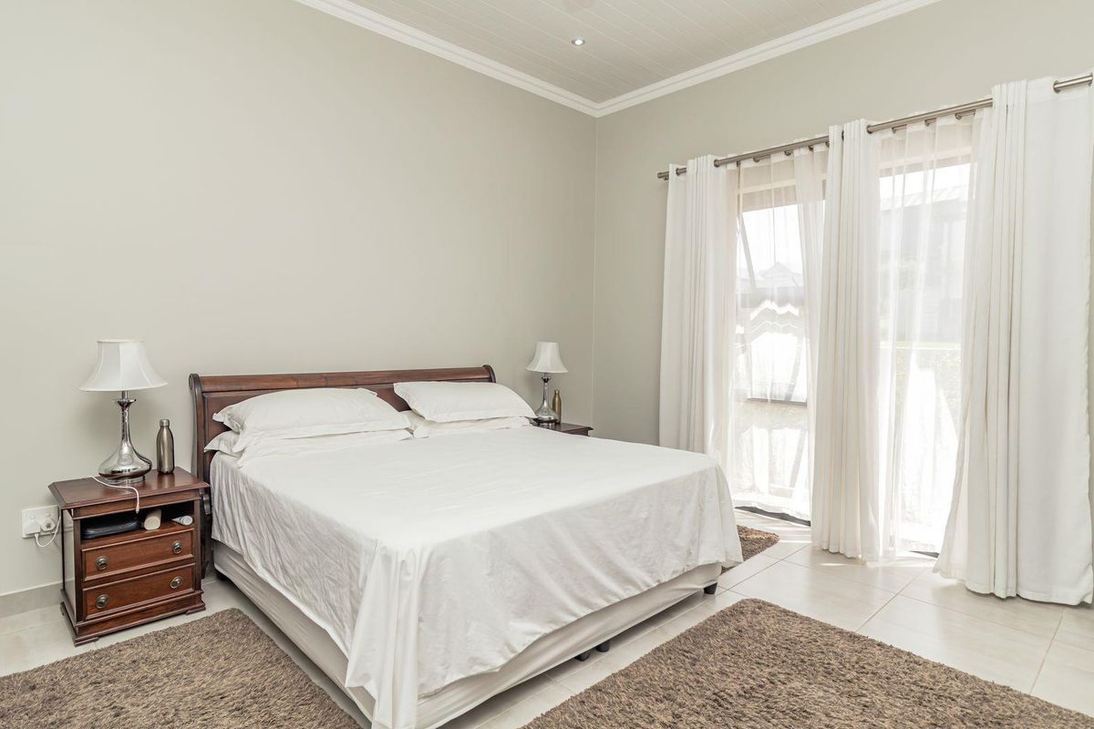 A bright and spacious bedroom featuring tiled flooring, crown molding, and large glass sliding doors that provide access to the outdoors.