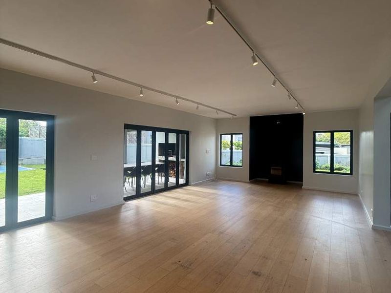 Spacious, light-filled living area featuring modern track lighting, light hardwood flooring, and large black-framed glass doors opening to the garden.