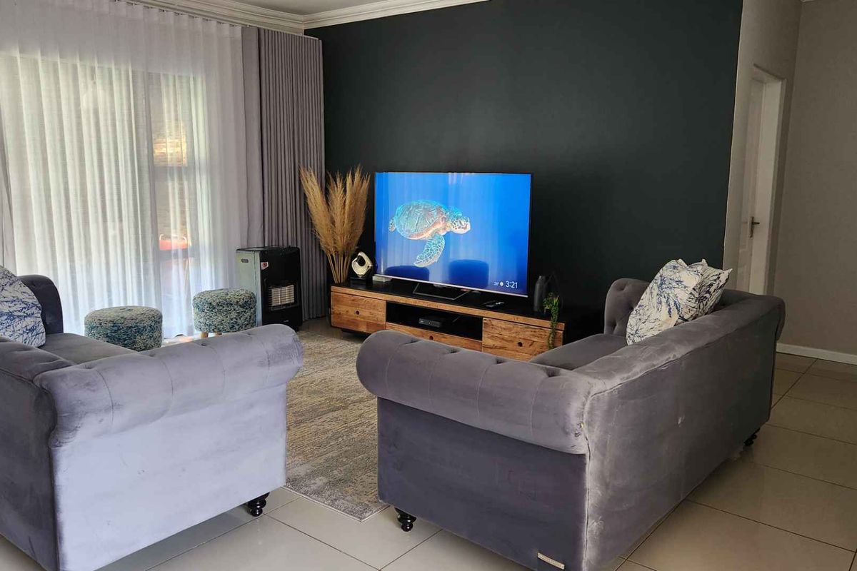 A comfortable living room featuring large sliding glass doors with floor-to-ceiling curtains, tiled flooring, and a dark accent wall.