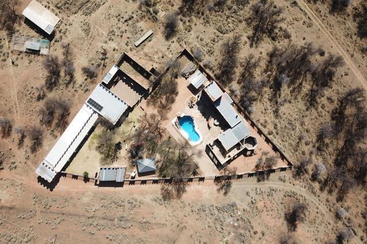 Aerial view of the small holding property featuring multiple structures, a swimming pool, and surrounding natural landscape.
