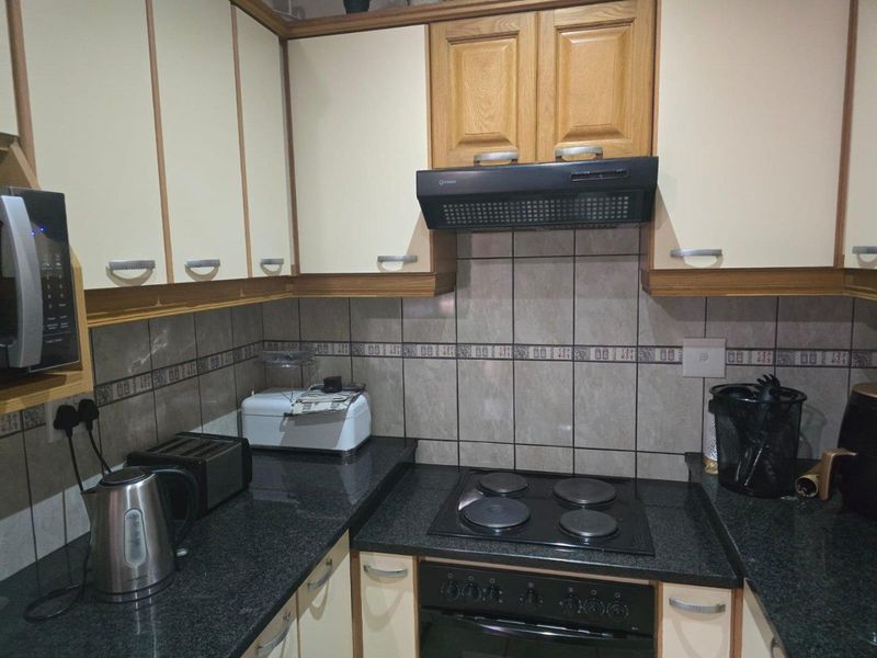 A functional kitchen featuring built-in cabinetry, granite countertops, a ceramic tile backsplash, and integrated appliances including an oven, hob, and extractor fan.