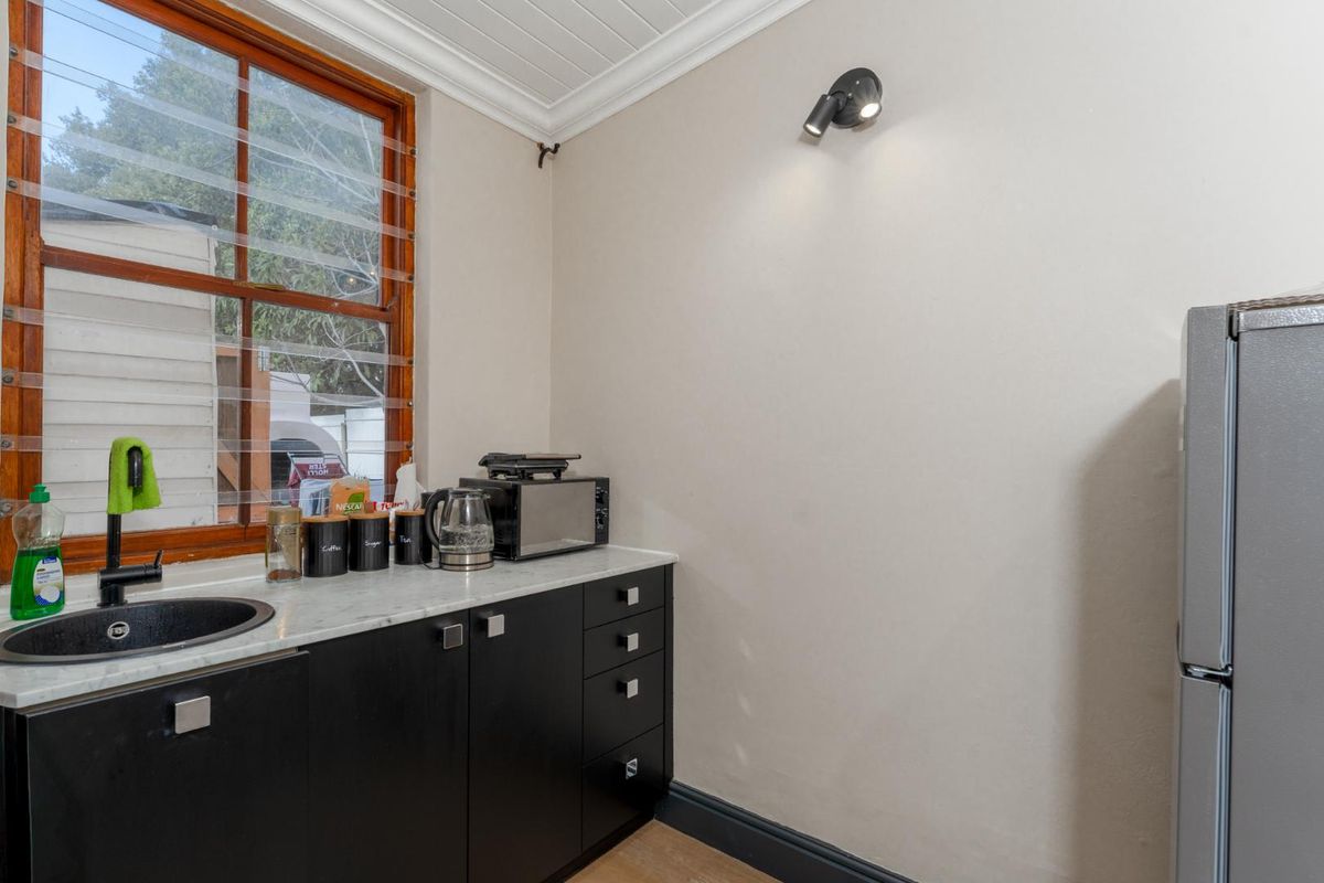 A compact office kitchenette featuring modern black cabinetry, a marble-effect countertop, a circular sink, and a wooden-framed window.