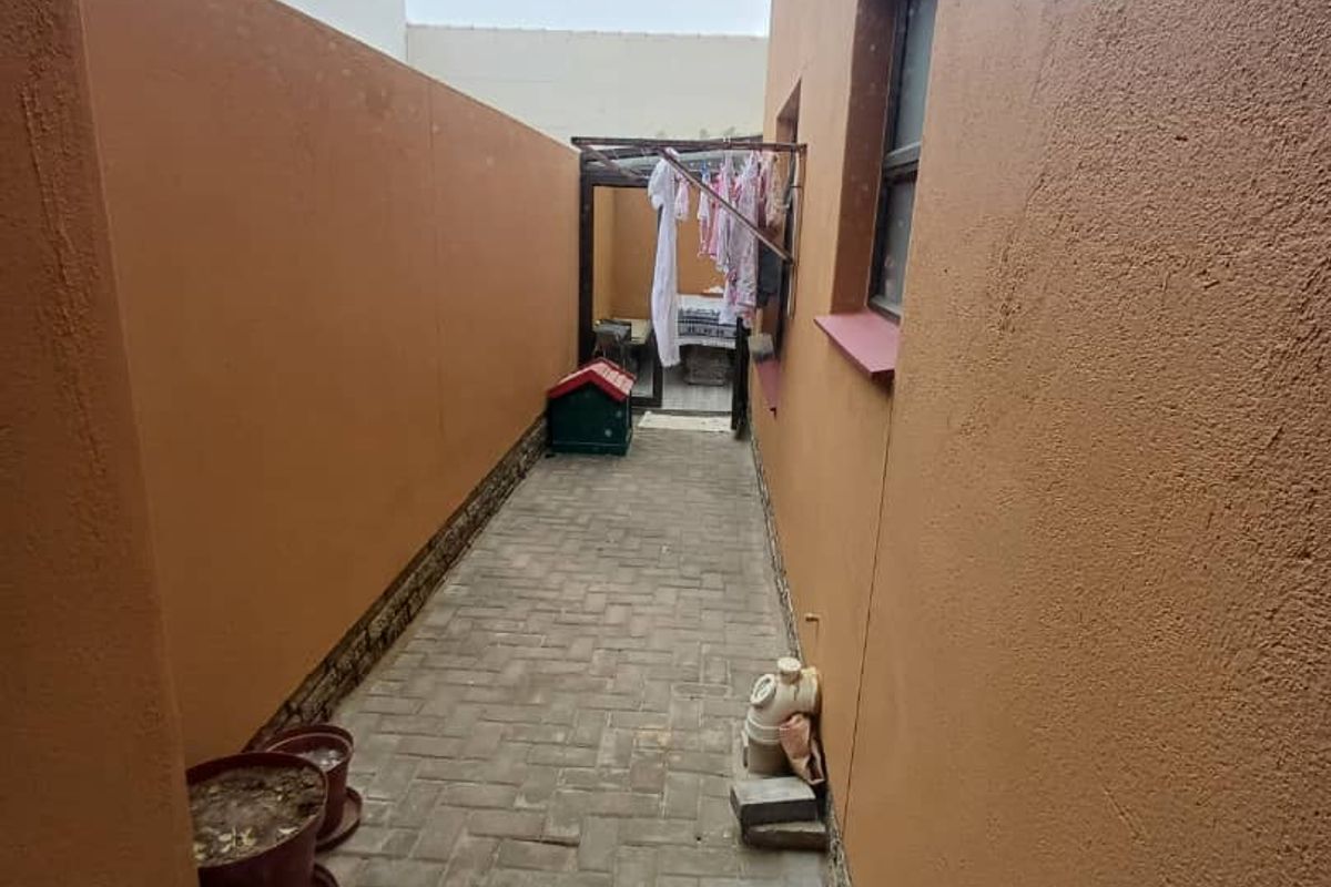 A narrow side passage featuring paved flooring and exterior wall access, providing a functional utility area along the side of the property.