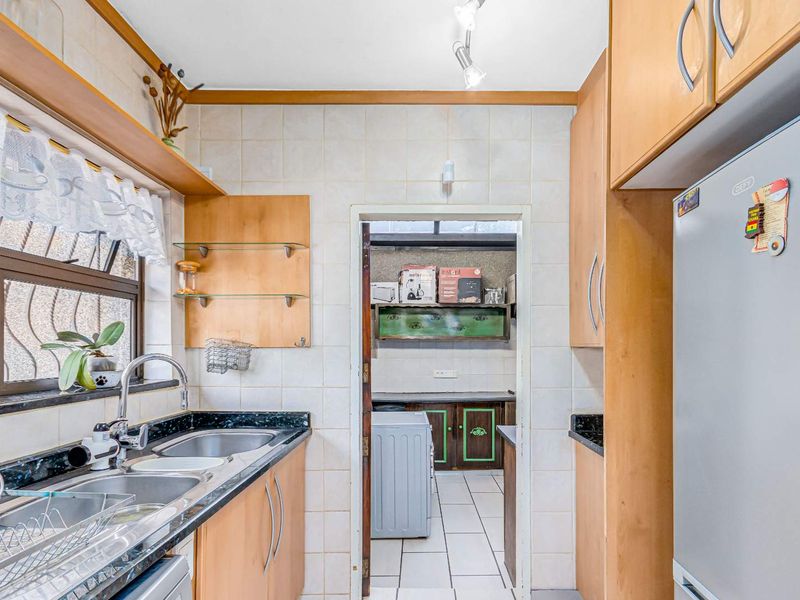 A functional kitchen featuring granite countertops, double basin sink, and built-in cabinetry, with an adjoining scullery area visible through the doorway.