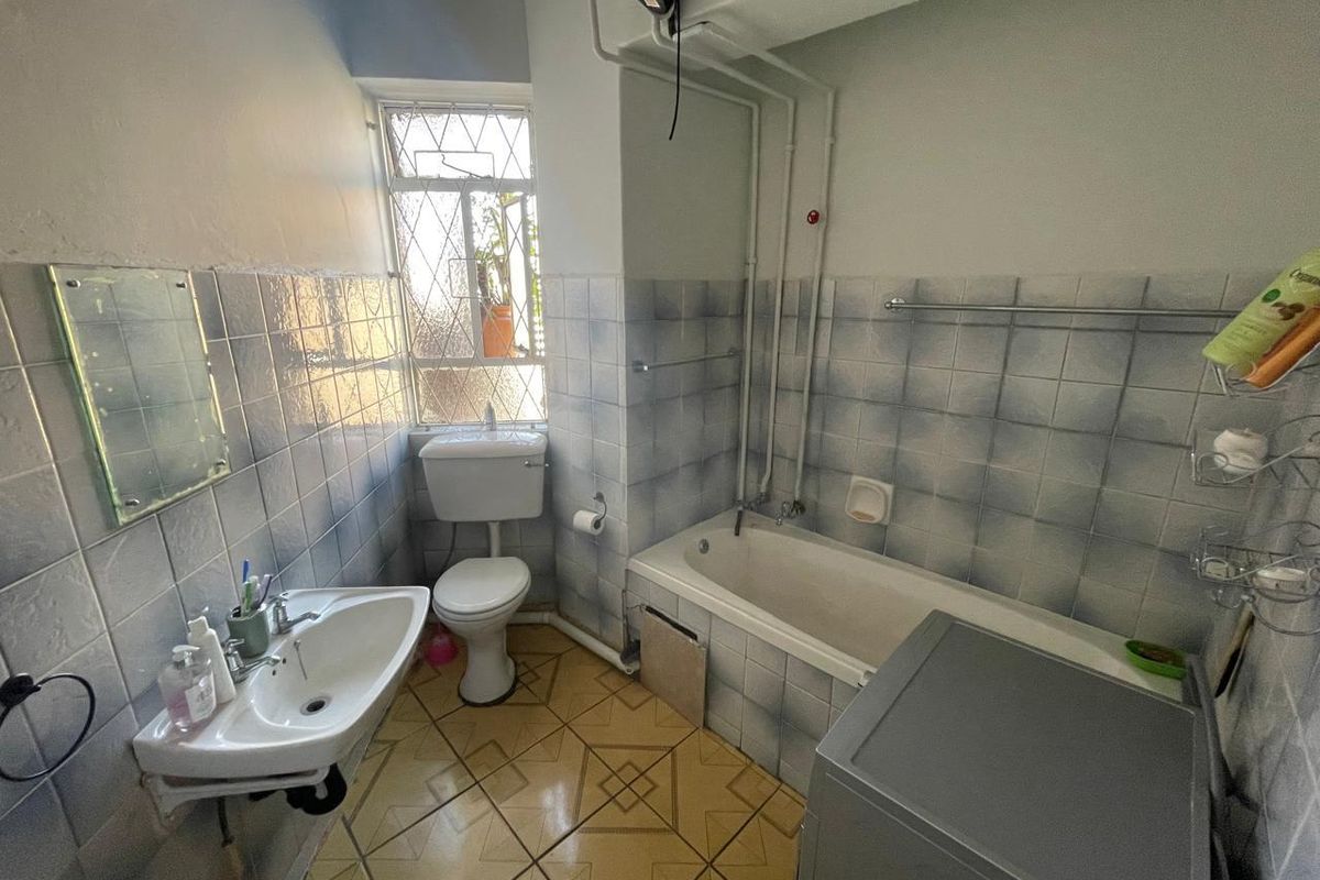 A dated bathroom featuring a bathtub, wall-mounted basin, and toilet, with exposed plumbing and original tile finishes throughout.