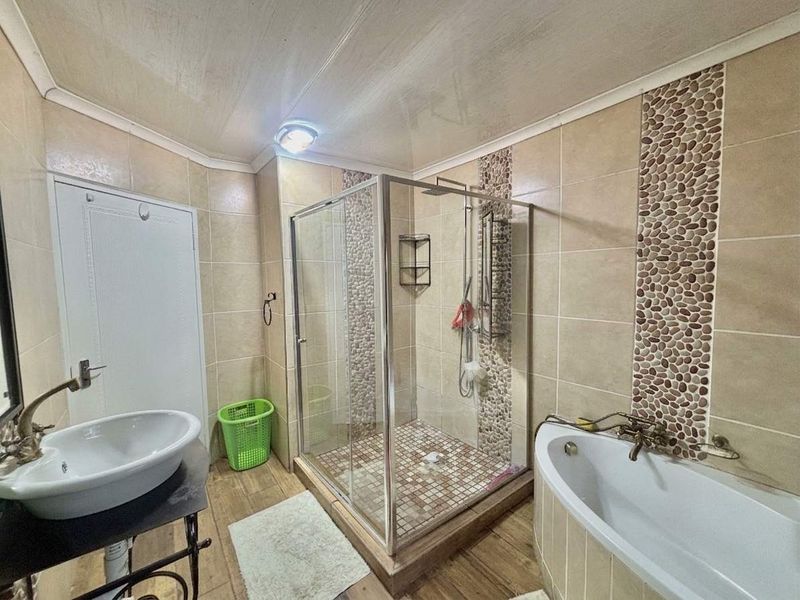 A bathroom featuring a glass-enclosed shower, a freestanding bathtub, and a vessel sink with decorative pebble tile accents on the walls.
