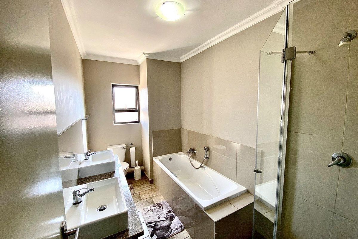 A modern bathroom featuring a double vanity, a built-in bathtub, and a separate glass-enclosed shower with neutral tiling.