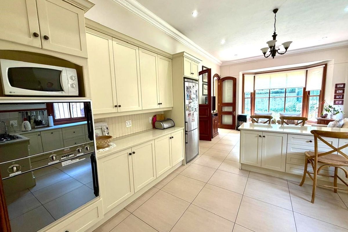 Spacious kitchen featuring cream cabinetry, a central island, tiled flooring, and a bright bay window area with integrated appliances.