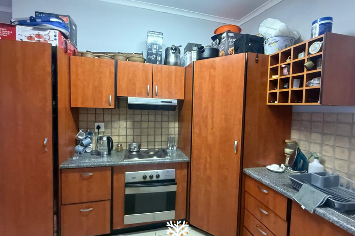 A functional kitchen featuring wood-veneer cabinetry, granite-look countertops, a built-in oven, and a hob with an extractor fan.