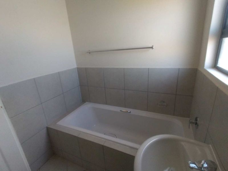 A clean, functional bathroom featuring a built-in bathtub with tiled surround, a pedestal basin, and a wall-mounted towel rail.