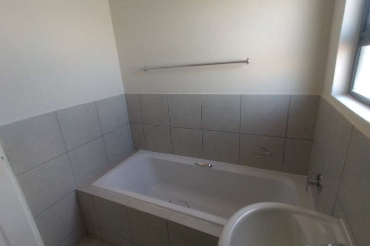 A clean, functional bathroom featuring a built-in bathtub with tiled surround, a pedestal basin, and a wall-mounted towel rail.