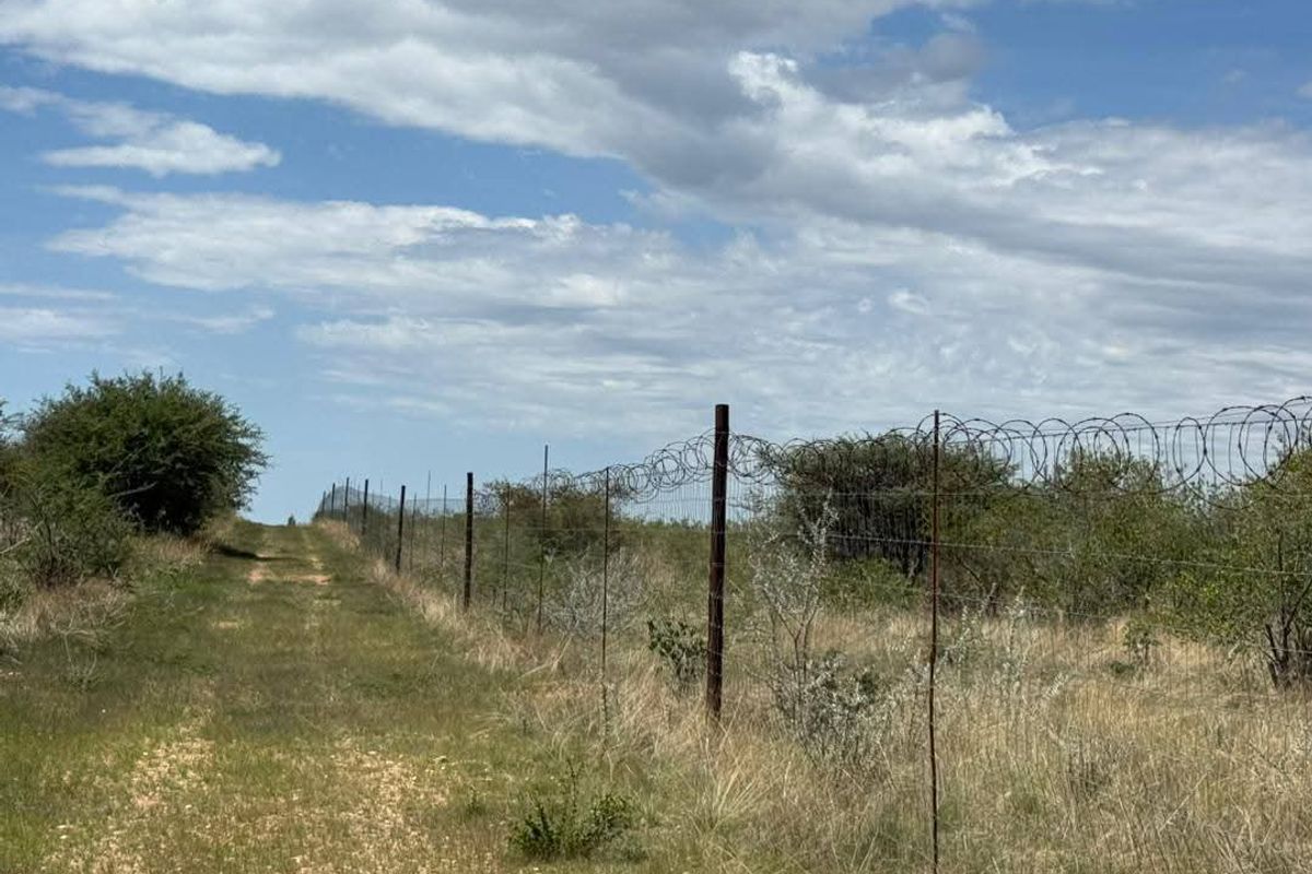 A view of the farm perimeter featuring a dirt track alongside a wire fence topped with razor wire.