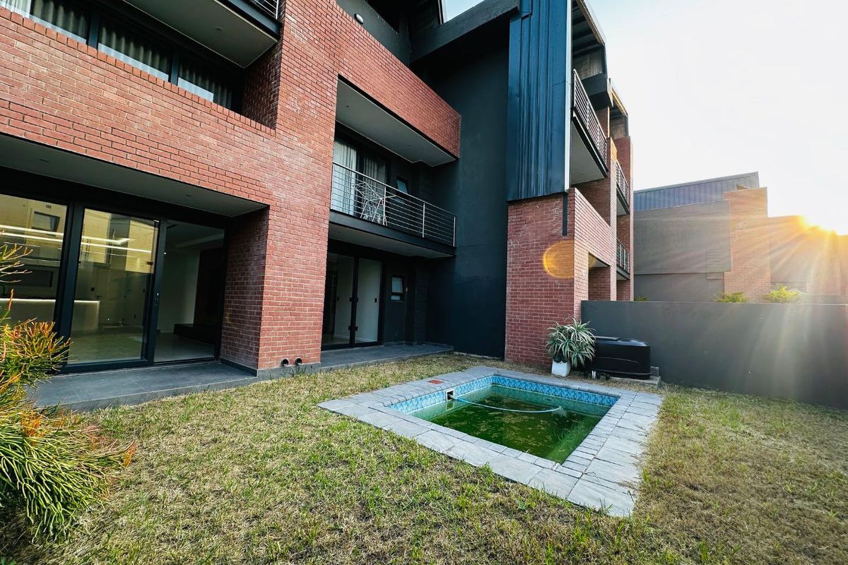 Rear view of a modern apartment building featuring a brick and dark metal facade, private balcony, and a small plunge pool in the garden area.