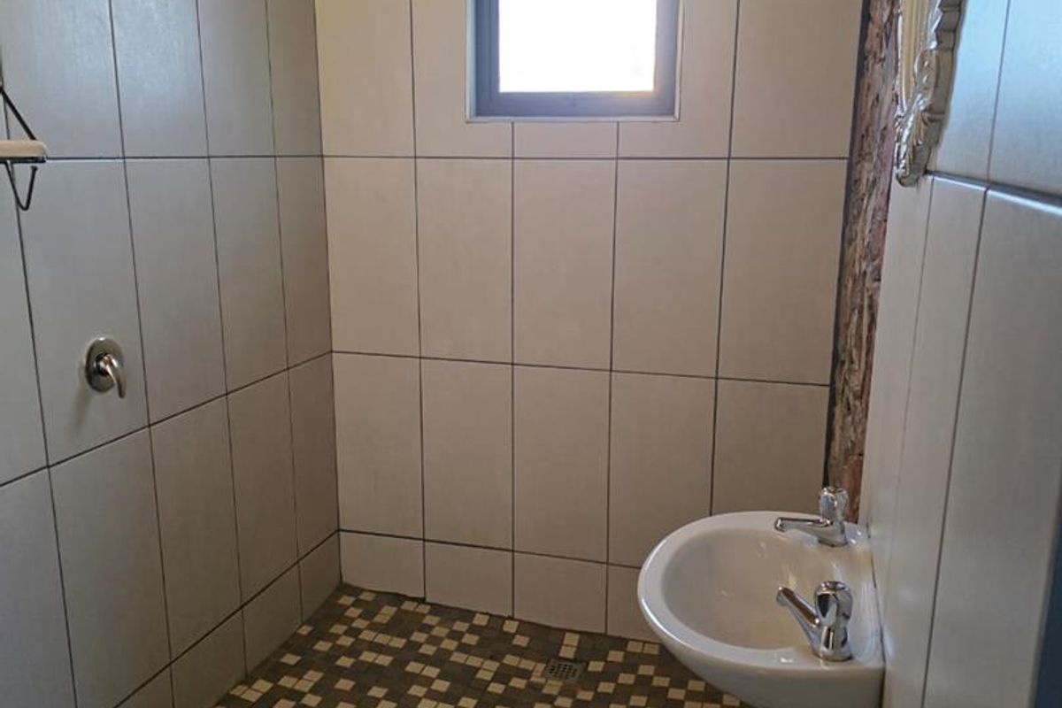 A functional bathroom featuring a shower area with tiled walls, a small basin, and a wooden ceiling finish.