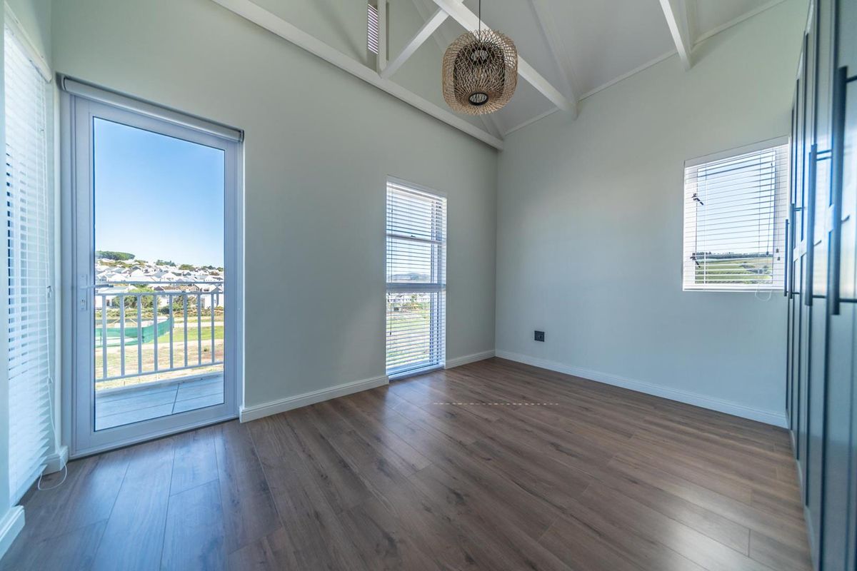 Bright and spacious bedroom featuring vaulted ceilings with exposed rafters, modern laminate flooring, built-in cupboards, and direct access to a private balcony.