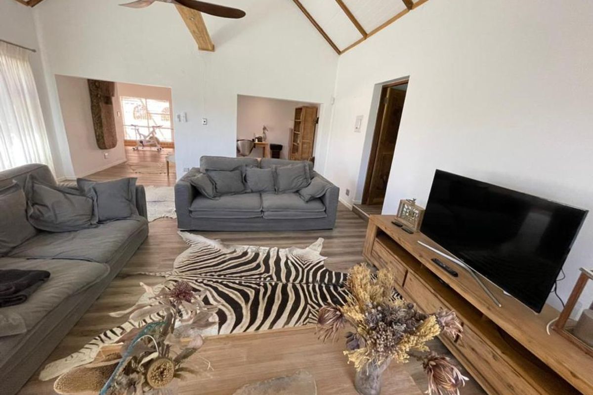 Spacious living room featuring high vaulted ceilings with exposed timber beams, wood-look flooring, and an open-plan layout connecting to adjacent rooms.