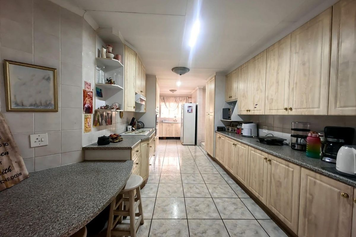A long galley-style kitchen featuring extensive laminate cabinetry, granite countertops, and ceramic floor tiles, offering ample storage and workspace.
