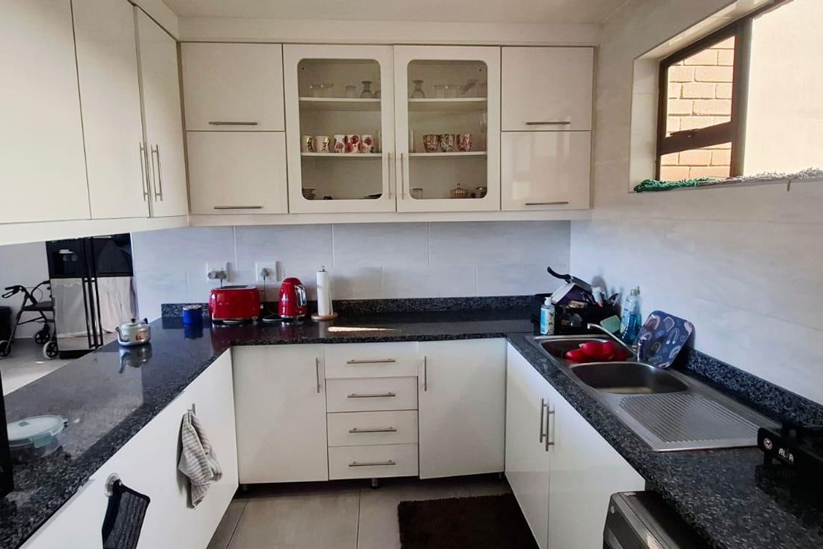 A functional kitchen featuring white cabinetry, granite countertops, a double stainless steel sink, and a tiled backsplash with ample storage space.