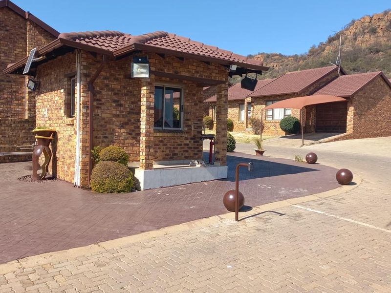 A well-maintained face brick security guard house situated at the entrance of a residential cluster complex with paved driveway and surrounding brick homes.