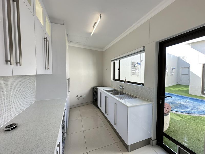 A clean, modern scullery featuring white cabinetry, stone countertops, a double sink, and direct access to the outdoor pool area.