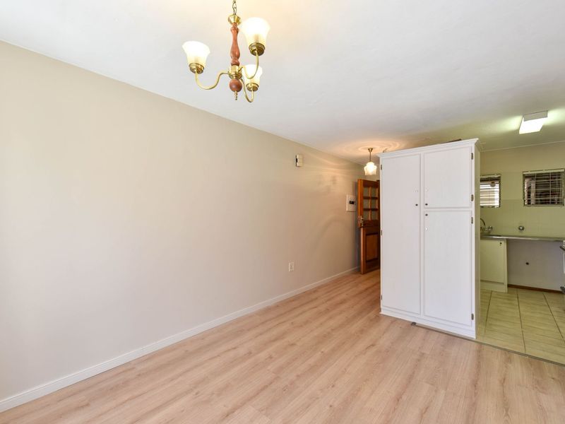 Open plan living area featuring light laminate flooring, neutral walls, and an adjoining kitchen space with built-in cabinetry and tiled finishes.