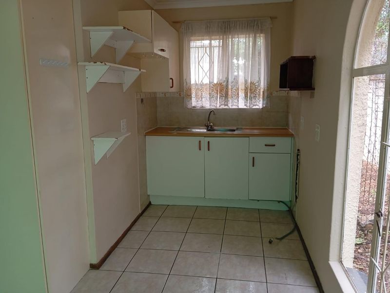A compact kitchen area featuring dated cabinetry, a stainless steel sink, tiled flooring, and an arched window providing natural light.