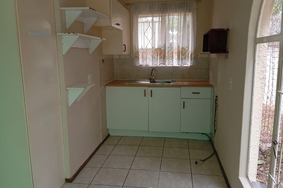 A compact kitchen area featuring dated cabinetry, a stainless steel sink, tiled flooring, and an arched window providing natural light.