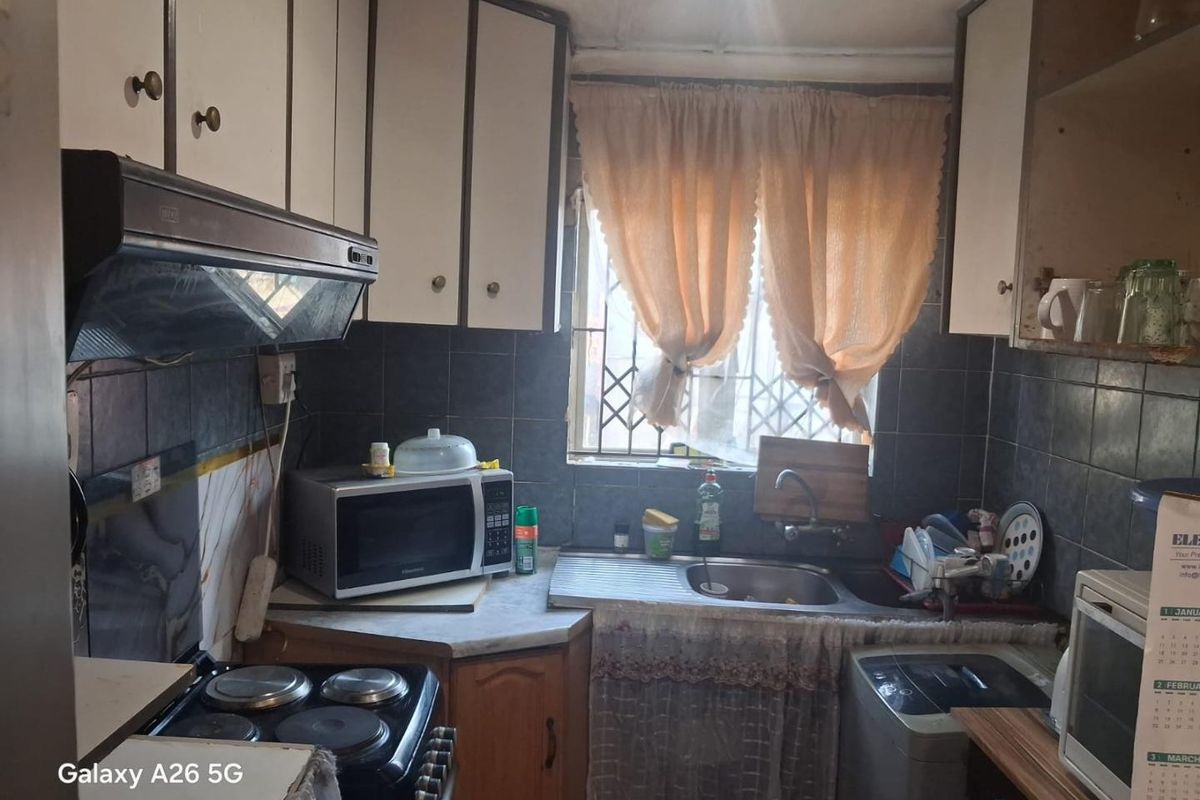 A compact, dated kitchen featuring built-in cabinetry, a stainless steel sink, and tiled backsplash, requiring modernization to improve functionality and aesthetic appeal.