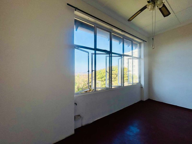 An empty bedroom featuring large aluminium-framed windows that provide natural light and views, complemented by a ceiling fan.