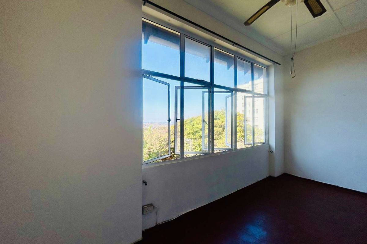 An empty bedroom featuring large aluminium-framed windows that provide natural light and views, complemented by a ceiling fan.