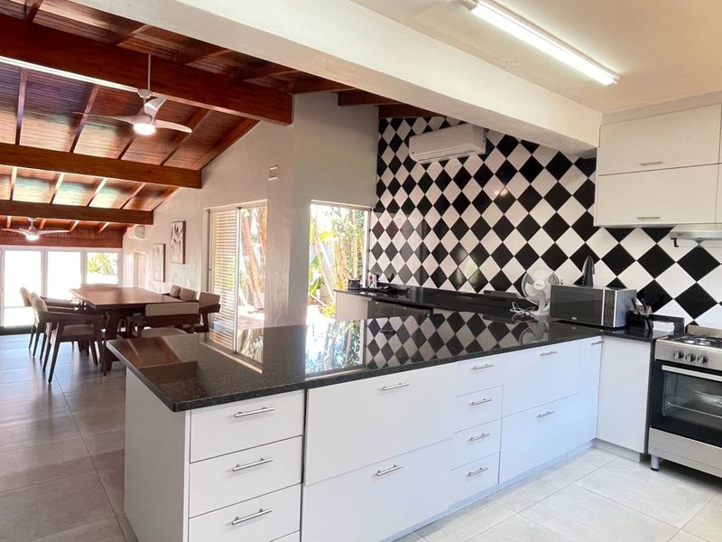 Spacious open-plan kitchen and dining area featuring exposed timber beams, modern white cabinetry, granite countertops, and direct access to the outdoor space.