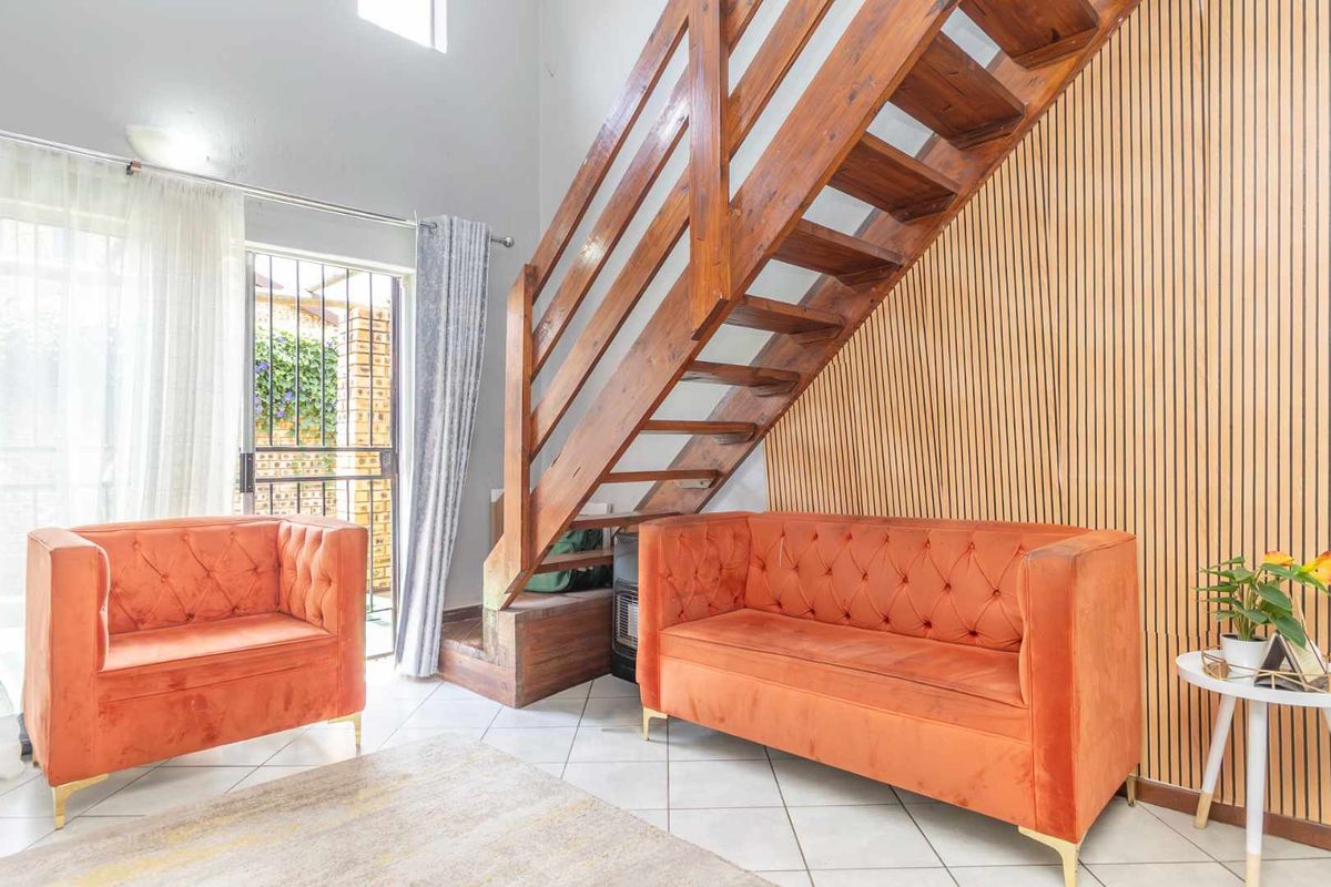 A bright living area featuring a prominent wooden staircase, modern slatted timber wall paneling, and tiled flooring with access to an outdoor area.