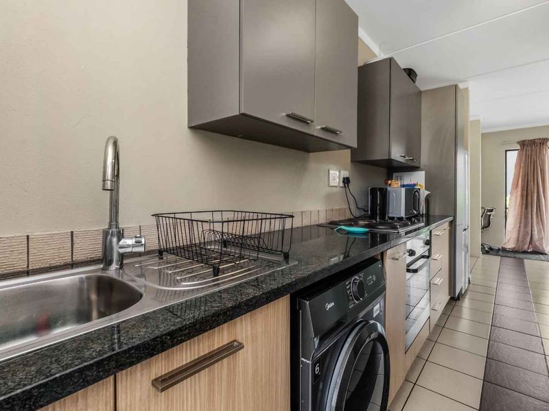 A functional galley-style kitchen featuring granite countertops, built-in cabinetry, integrated oven and hob, and tiled flooring, leading towards an adjacent living area.