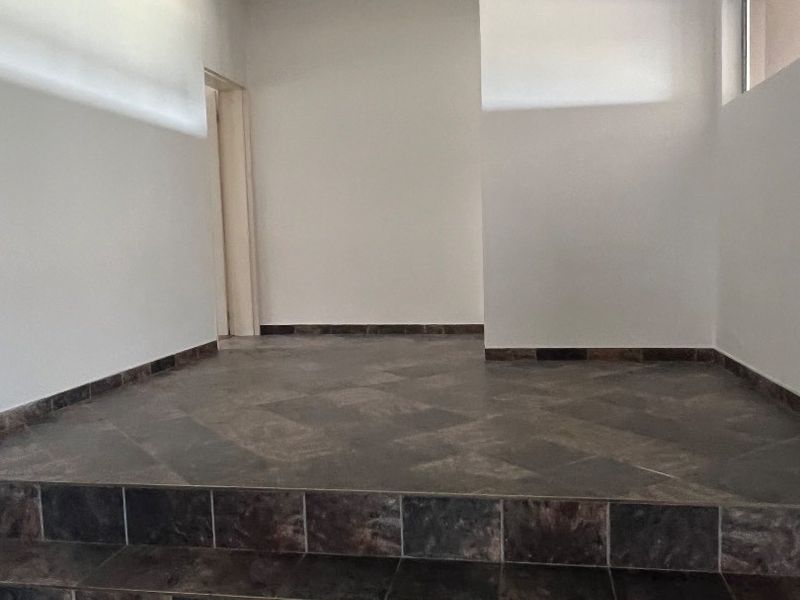 An empty entrance area featuring dark tiled flooring with a stepped transition and neutral wall finishes.