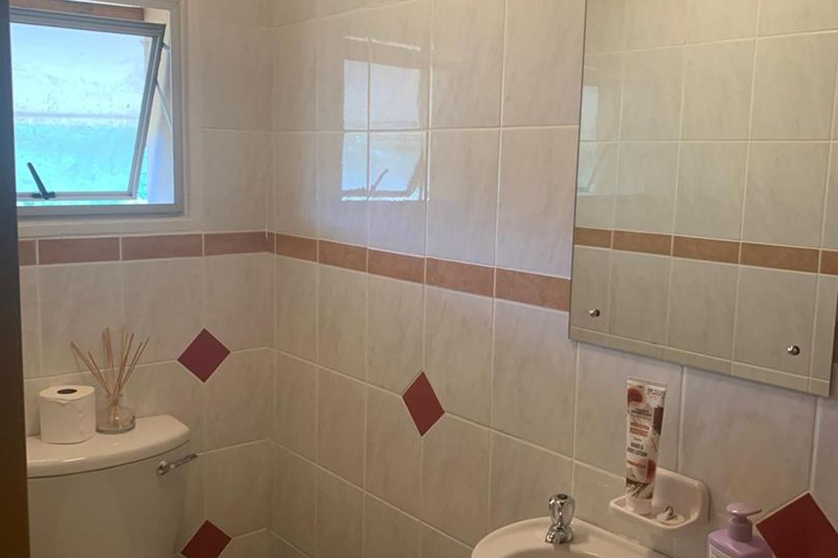 A compact bathroom featuring a wall-mounted basin, a standard toilet, and tiled walls with a timber-clad ceiling.
