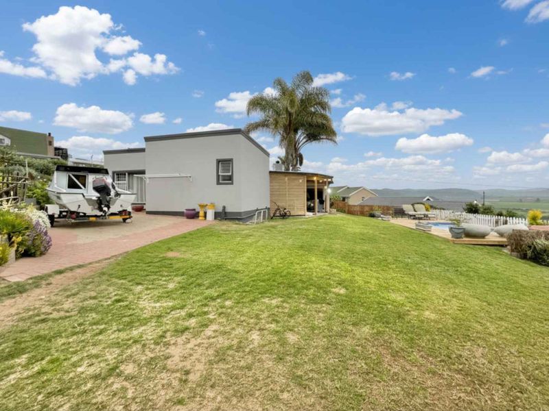 Rear exterior view featuring a spacious lawn, paved driveway, swimming pool with wooden decking, and surrounding fencing.