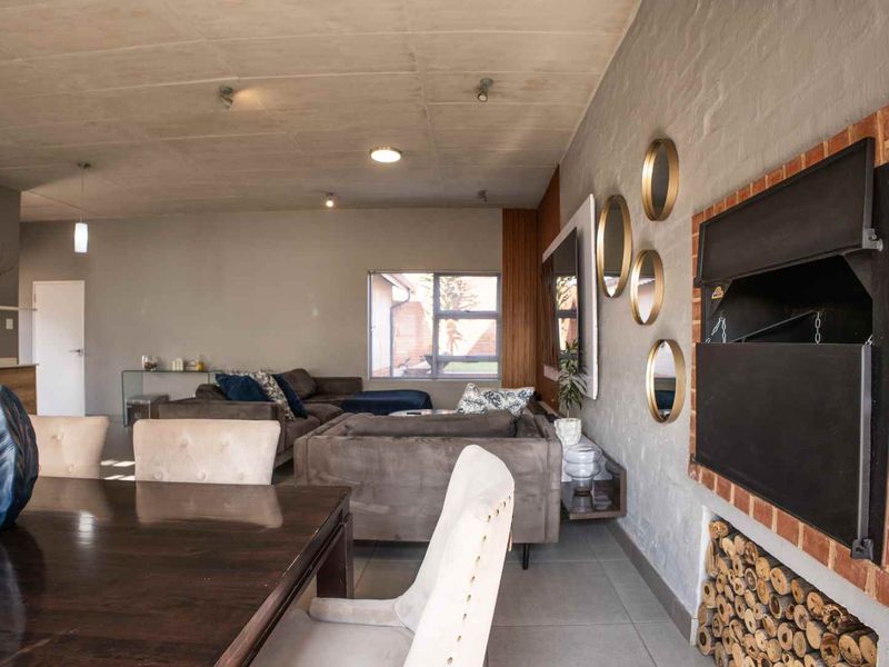 Spacious open-plan living and dining area featuring an exposed concrete ceiling, tiled floors, and a prominent built-in fireplace with a brick surround.