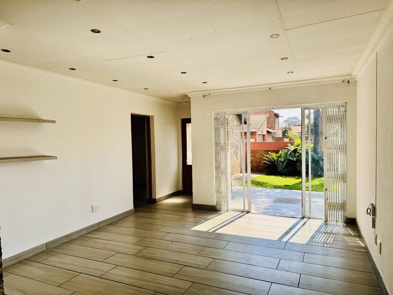A bright, empty living area featuring modern tiled flooring, recessed lighting, and a sliding glass door providing direct access to the rear patio and garden.