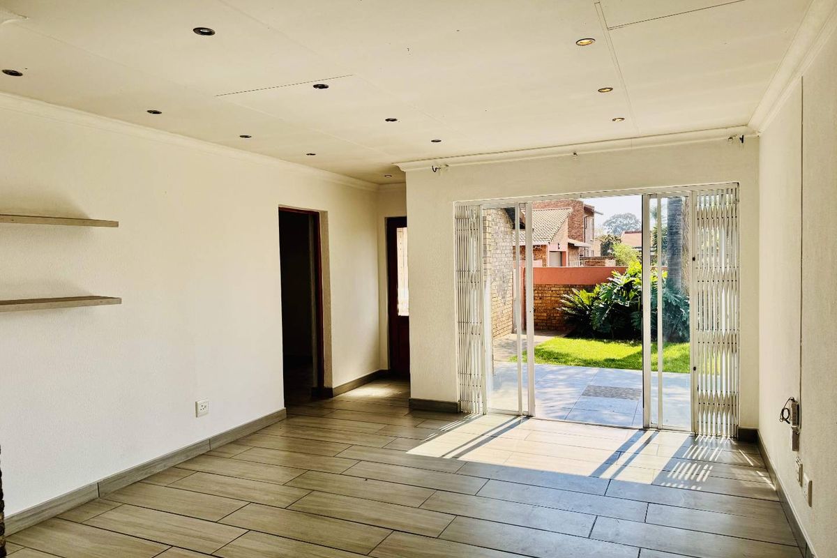 A bright, empty living area featuring modern tiled flooring, recessed lighting, and a sliding glass door providing direct access to the rear patio and garden.