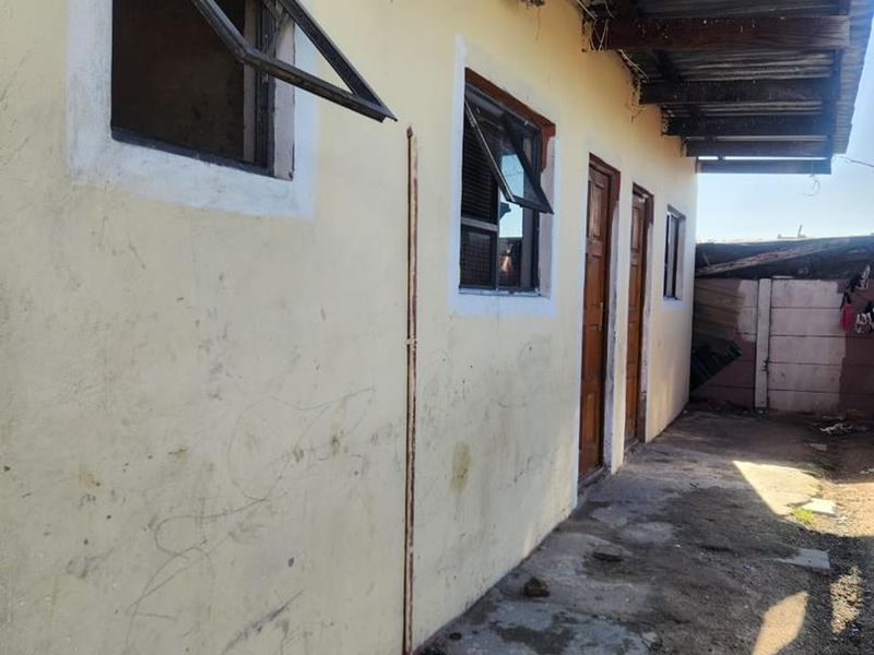 Rear exterior view of the property showing weathered walls, timber door frames, and a corrugated metal roof structure requiring maintenance.
