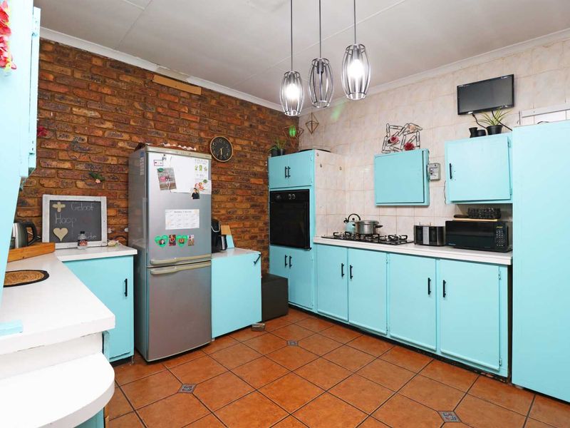 A functional kitchen featuring exposed brick walls, tiled flooring, built-in cabinetry, and integrated cooking appliances including an oven and gas hob.