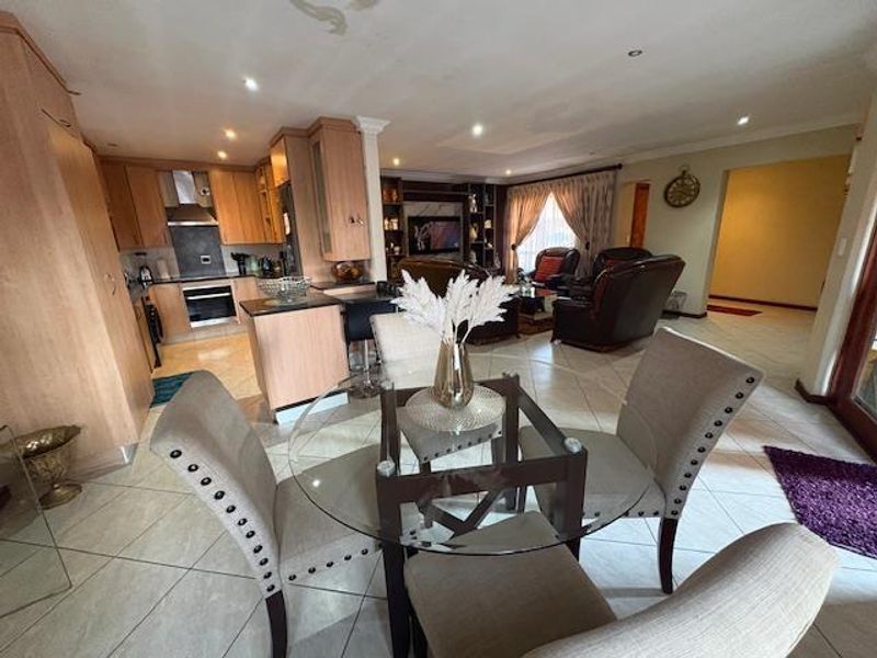 Open-plan living area featuring a kitchen with built-in cabinetry and appliances, flowing into a dining space and lounge with tiled flooring throughout.