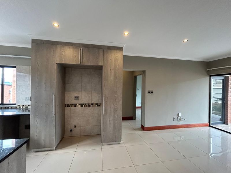 An open-plan living area featuring modern tiled flooring, recessed lighting, and built-in cabinetry, with access to an outdoor balcony through a sliding glass door.