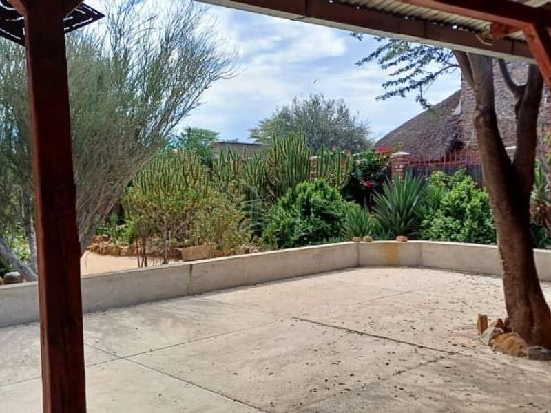 A covered outdoor patio area featuring a concrete floor, timber support beams, and a built-in concrete retaining wall overlooking a landscaped garden.