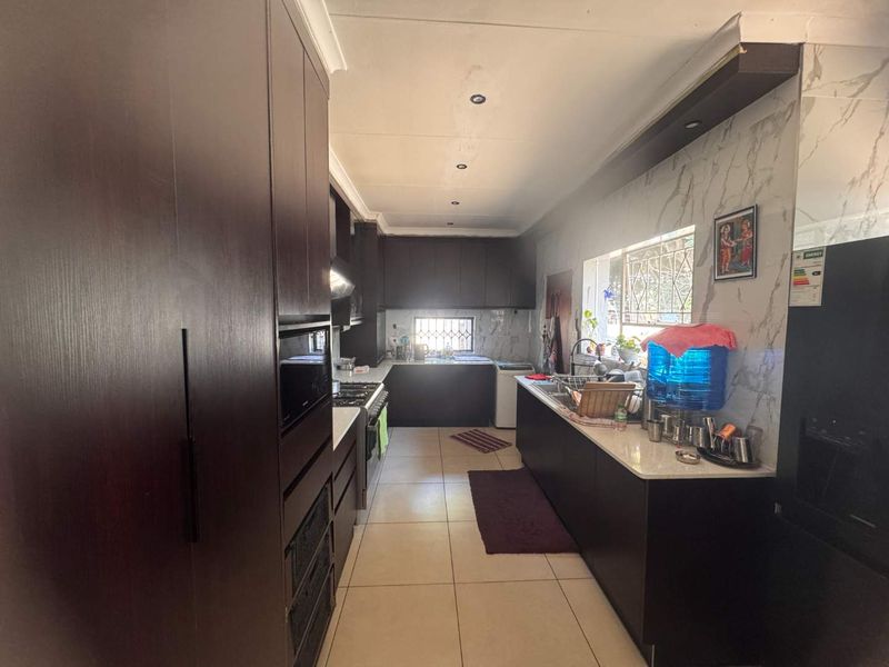 A functional galley-style kitchen featuring dark wood cabinetry, stone countertops, marble-look splashbacks, and integrated appliances with tiled flooring throughout.